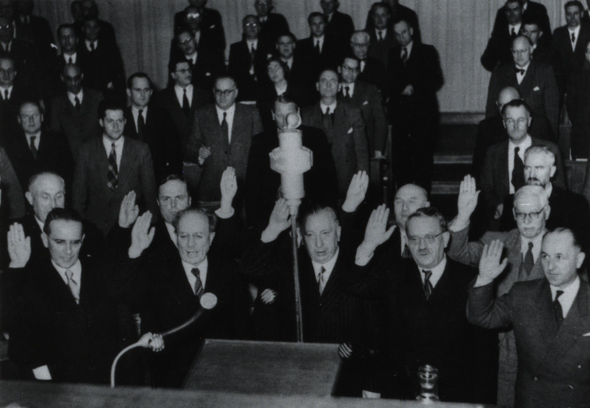 Vereidigung der neuen Regierungsmitglieder des Kabinetts Ehard III am 18. Dezember 1950 im Bayerischen Landtag. Vordere Reihe von l.n.r.: Arbeitsminister Richard Oechsle (SPD), Innenminister und Stv. Ministerpräsident Wilhelm Hoegner (SPD), Justizminister Josef Müller (CSU), Landwirtschaftsminister Alois Schlögl (CSU), Wirtschaftsminister Hanns Seidel (CSU), hintere Reihe von l.n.r.: Wirtschaftsstaatssekretär Willi Guthsmuths (BHE), Innenstaatssekretär für das Flüchtlingswesen Theodor Oberländer (BHE), Landwirtschaftsstaatssekretär Johann Maag (SPD, im Bild verdeckt), Arbeitsstaatssekretär Heinrich Krehle (CSU), Finanzstaatssekretär Richard Ringelmann (parteilos). Justizstaatssekretär Fritz Koch (CSU) war in der Landtagssitzung vom 18. Dezember nicht anwesend und wurde am darauffolgenden Tag vereidigt. Erst am 3. Januar 1951 war das Kabinett mit der Vereidigung von Kultusminister Josef Schwalber, Kultusstaatssekretär Eduard Brenner (SPD), Finanzminister Wolfgang Zorn (SPD) und Innenstaatssekretär Paul Nerrter (CSU) vollständig.<br/>Nachweis: Bayerisches Landtagsarchiv