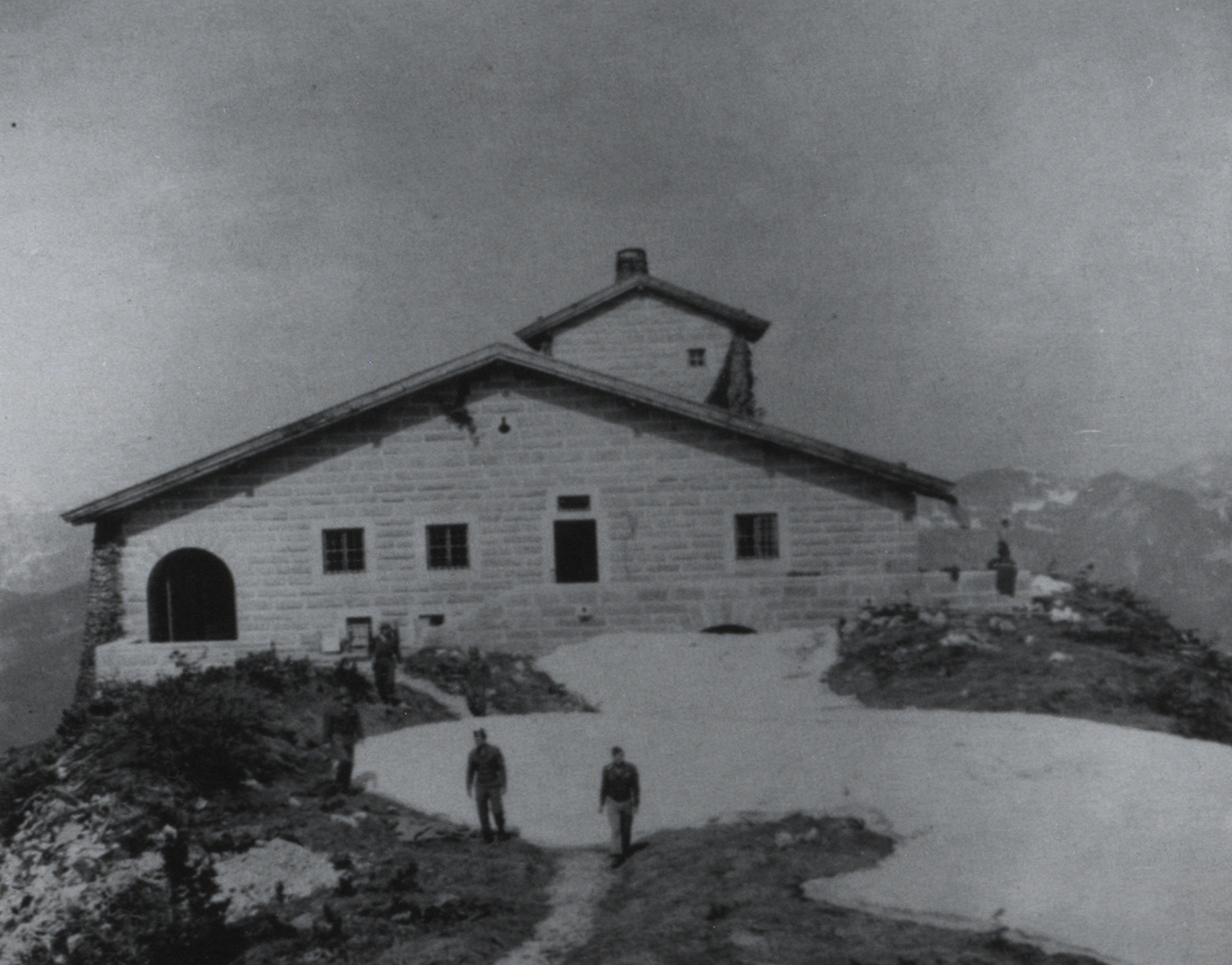 Angehörige der US-Army vor dem Teehaus auf dem Kehlstein bei Berchtesgaden. Aufnahme unbekannten Datums, vermutlich Frühjahr/Sommer 1945. Das Gebäude auf dem Kehlstein, errichtet 1938/39 im Auftrag Martin Bormanns, war ein Geschenk der NSDAP an Adolf Hitler zu dessen 50. Geburtstag am 20. April 1939 gewesen. Im Jahre 1951 gab die US-Besatzungsmacht das beschlagnahmte Gebäude, die dazugehörige Zufahrtsstraße wie auch das sogenannte ‚Führersperrgebiet‘ auf dem Obersalzberg an die bayerische Staatsverwaltung zurück. Der Ministerrat hatte eine Entscheidung über die künftige Nutzung des Kehlsteinhauses zu fällen; das primäre Interesse der Staatsregierung war dabei zunächst, die Entstehung einer nationalsozialistischen Kult- oder Pilgerstätte zu unterbinden. Ab 1952 wurde das Kehlsteinhaus vom Freistaat an den Deutschen Alpenverein Sektion Berchtesgaden verpachtet, seit 1962 liegt das Nutzungsrecht bei der gemeinnützigen Berchtesgadener Landesstiftung, die Verwaltung und Unterverpachtung des Kehlsteinhauses obliegt dem Fremdenverkehrsverband Berchtesgaden.<br/>Nachweis: BayHStA Abt. V Bildersammlung 634