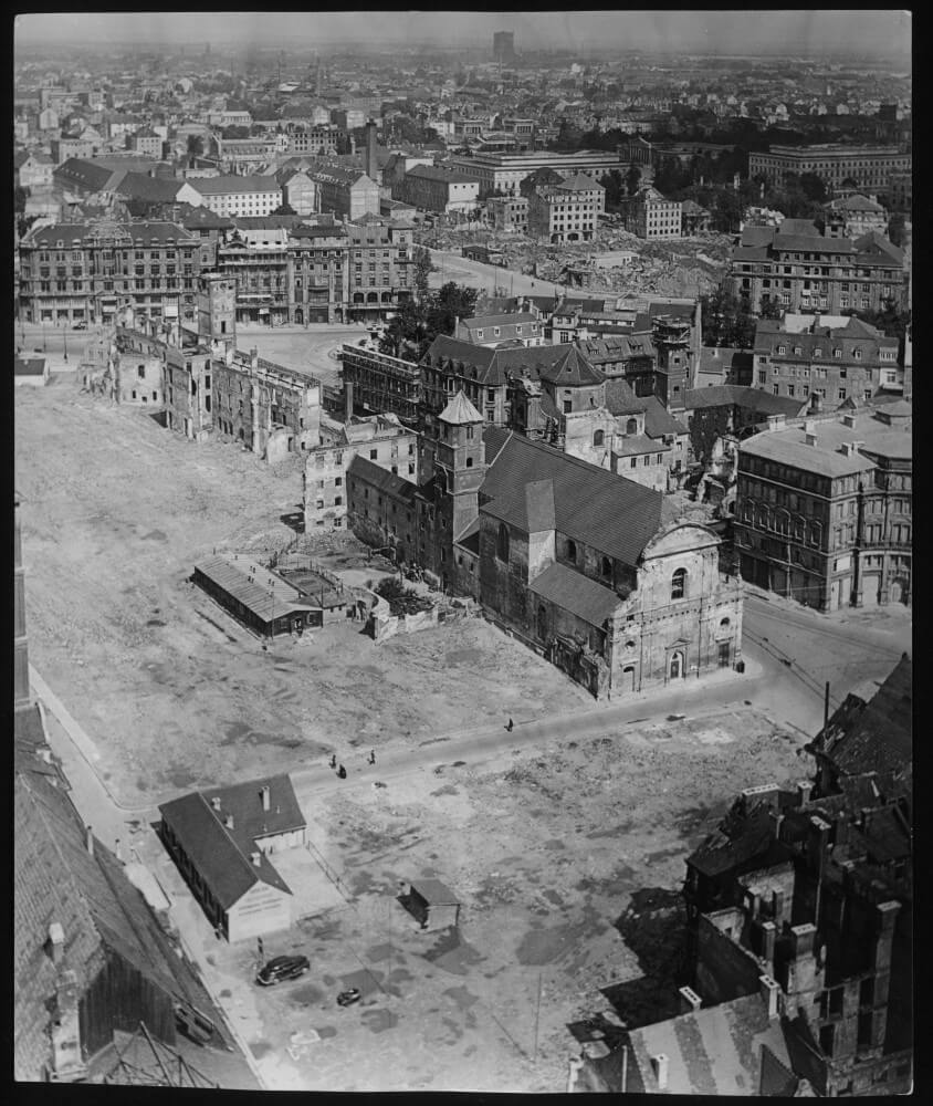 Das geräumte Maxburg-Gelände zwischen Lenbachplatz, Pacellistraße und Maxburgstraße in München, aufgenommen im Jahre 1951 vom nördlichen Turm der Frauenkirche. Im Vordergrund die kriegbeschädigte Kamelitenkirche. Zwei Jahre später waren auch die alten Mauerrest um den noch bestehenden Renaissanceturm abgetragen. Im Ministerrat wurden im Jahre 1953 wiederholt die Pläne und Modalitäten des Wiederaufbaus des repräsentativen, im Herzen Münchens gelegenen Areals diskutiert. Konflikte gab es insbesondere über die Finanzierung des Wiederaufbaus wie über die künftige Nutzung des neuen Gebäudekomplexes, der schließlich zwischen 1954 und 1957 nach Plänen der Architekten Sep Ruf und Theo Pabst erbaut wurde.<br/>Nachweis: Stadtarchiv München FS-NK-STB-34-06. © Bildverlag Prugger, München.