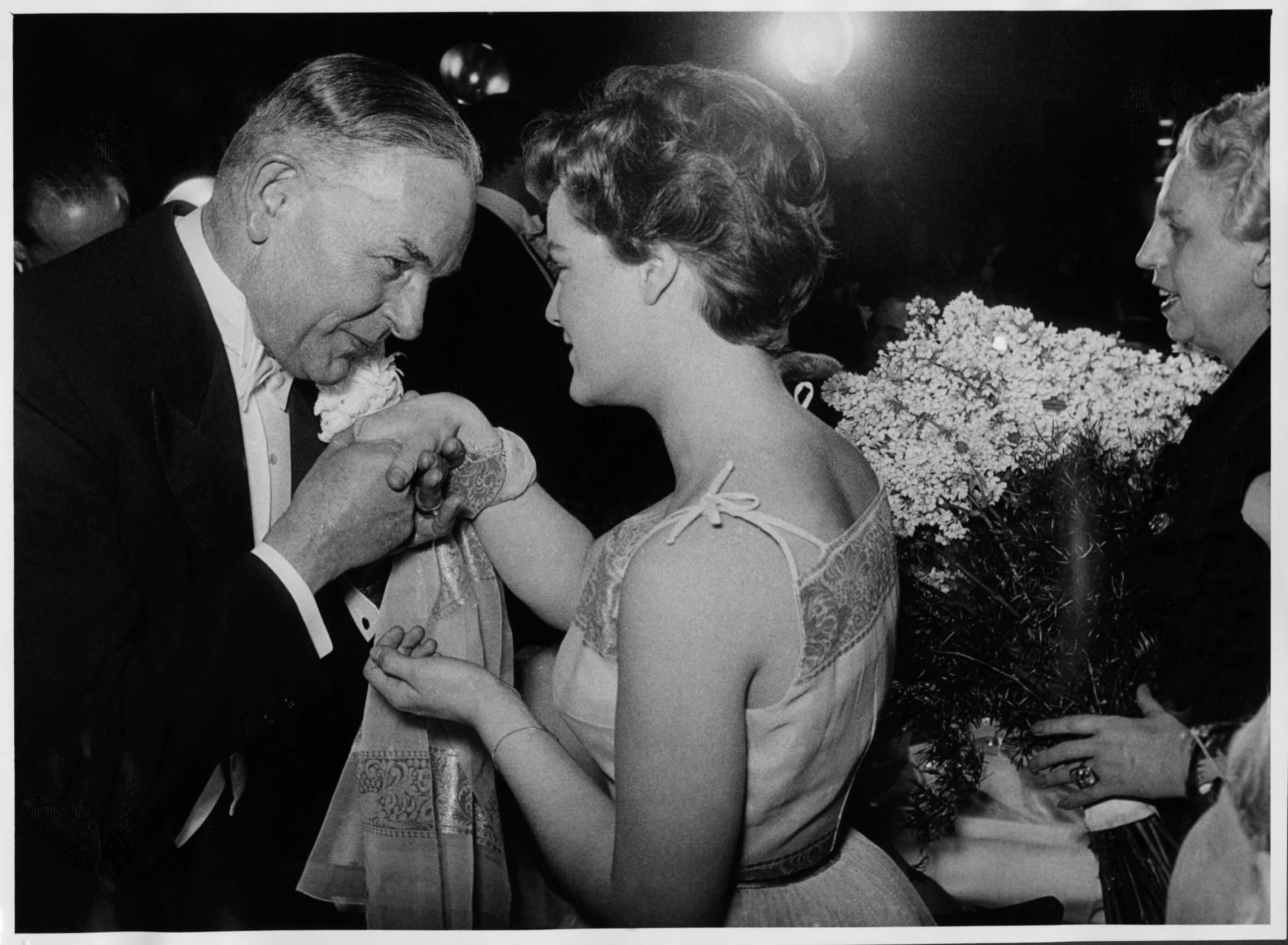 Ministerpräsident Hans Ehard mit Romy Schneider auf dem 30. Chrysanthemenball im Deutschen Theater in München am 5. Februar 1954, rechts im Bild sichtbar Ehards Ehefrau Annelore. Diese Traditionsveranstaltung der Münchner Faschingssaison war gleichzeitig Teil des großen gesellschaftlichen Rahmenprogramms, das die Ministerpräsidentenkonferenz vom 5. und 6. Februar begleitete. Auf Anregung der Ministerpräsidenten Hans Ehard (Bayern), Karl Arnold (Nordrhein-Westfalen) und Gebhard Müller (Baden-Württemberg) vom Dezember 1953 kam es Anfang Februar in München zu einem Treffen sämtlicher westdeutscher Regierungschefs, auf dem insbesondere kulturpolitische Themen wie die  Schul- und Erziehungspolitik oder Rundfunkfragen diskutiert wurden. Vgl. die Beiträge in der SZ Nr. 31, 8.2.1954, „Zehn Länderchefs erzielen Einvernehmen“, „Sie tranken noch ein Tröpfchen, aber nicht aus Henkeltöpfchen“ u. „München: Reigen um die Chrysantheme“.  <br/>Nachweis: NL Ehard 812