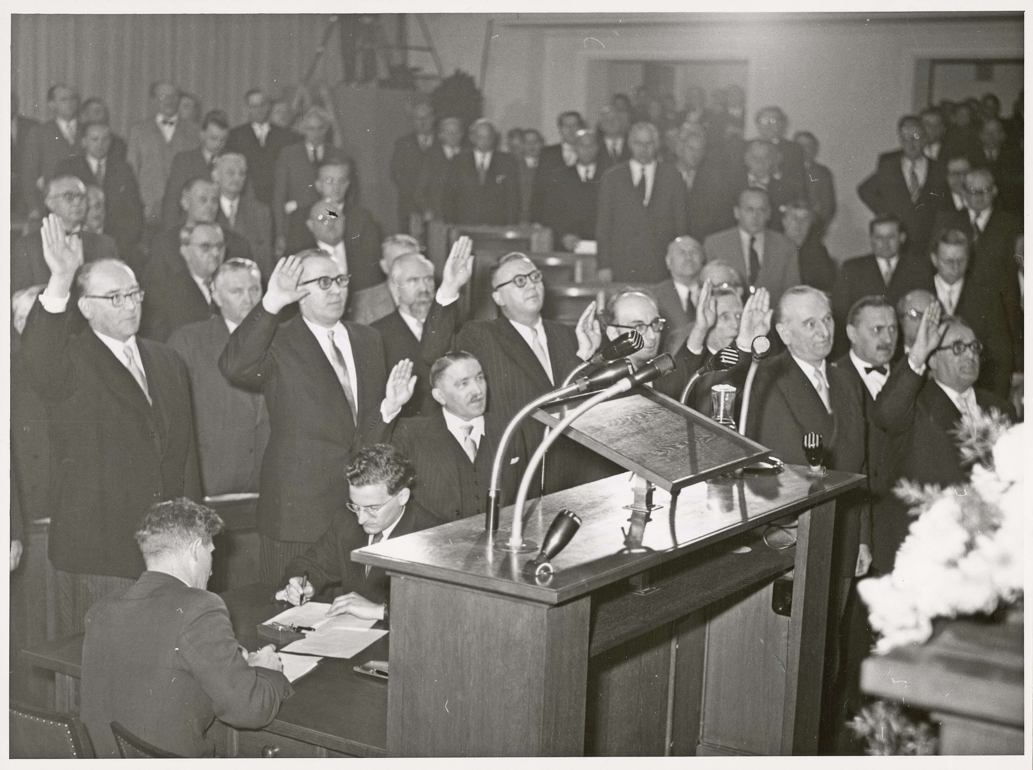 Die Vereidigung der neuen Kabinettsmitglieder der Viererkoalition in der Sitzung des Bayerischen Landtags vom 14. Dezember 1954.<br/>Von links nach rechts: Justizminister Fritz Koch, Finanzminister Friedrich Zietsch, Innenminister August Geislhöringer, Staatssekretär Eilles, Kultusminister August Rucker, Kultusstaatssekretär Hans Meinzolt, Wirtschaftsminister Otto Bezold, Finanzstaatssekretär Joseph Panholzer, Landwirtschaftsminister Joseph Baumgartner.<br/>Nachweis:Nicht abgebildet sind Arbeitsminister Walter Stain, der Leiter der Staatskanzlei und Staatssekretär Albrecht Haas, Innenstaatssekretär Ernst Vetter, Wirtschaftsstaatssekretär Willi Guthsmuths, Landwirtschaftsstaatssekretär Erich Simmel und der Staatssekretär im Arbeitsministerium Karl Weishäupl.<br/>Nachweis: StK-Fotos 110