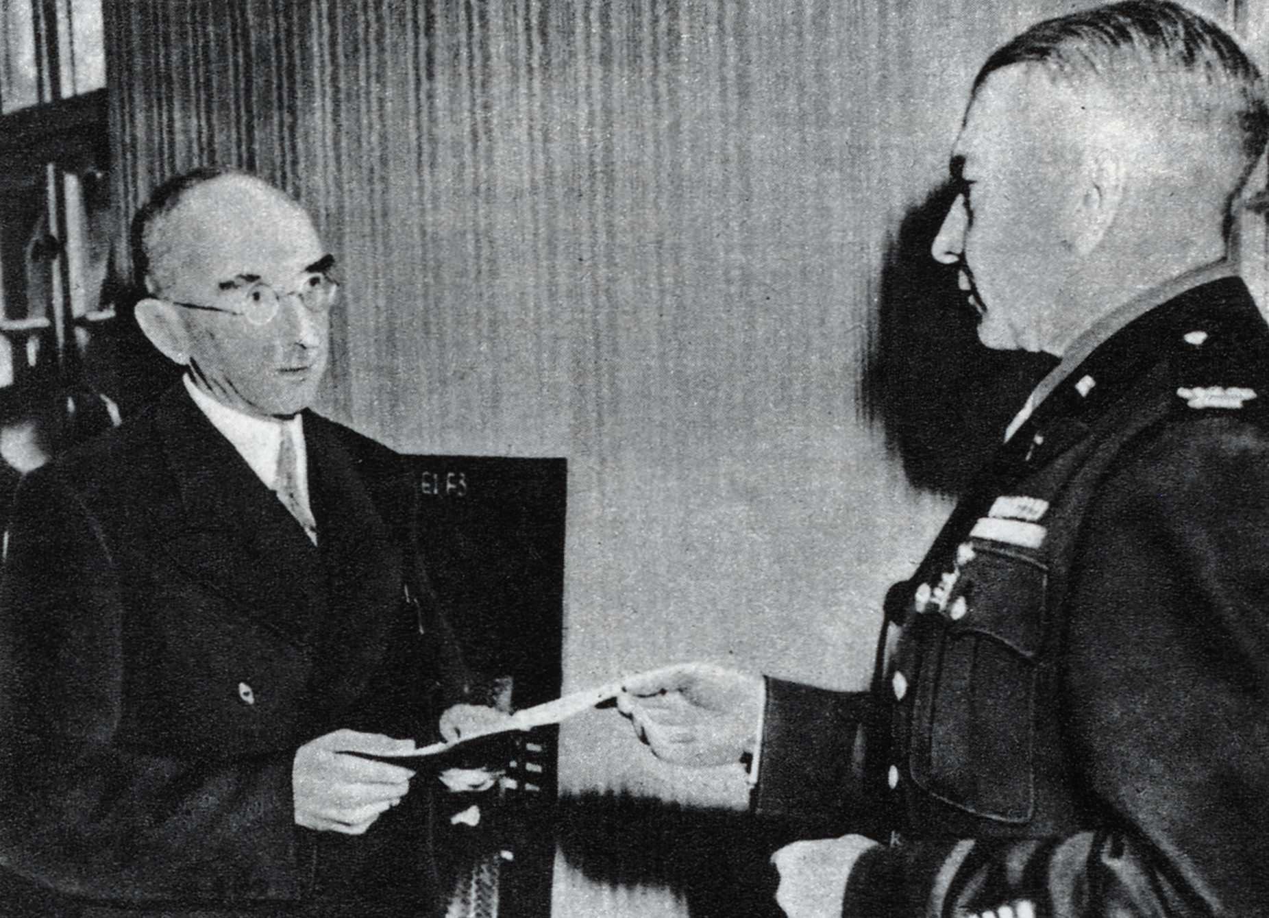 Am 28. Mai 1945 erhielt Fritz Schäffer von Colonel Charles E. Keegan die Ernennungsurkunde zum „Temporary Minister-Präsident for Bavaria“. Die Ernennung fand im Hauptquartier des Detachment E1F3 in der Holbeinstraße 11 in München statt (das Signet E1F3 befindet sich auf dem im Hintergrund des Photos erkennbaren Schreibtischstuhl Keegans).<br/>Nachweis: Vorlage von Frau Gisa Schäffer-Huber, Passau | Copyright Burda-Verlag/Frankfurter Illustrierte